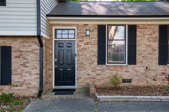 view of exterior entry with brick siding and crawl space
