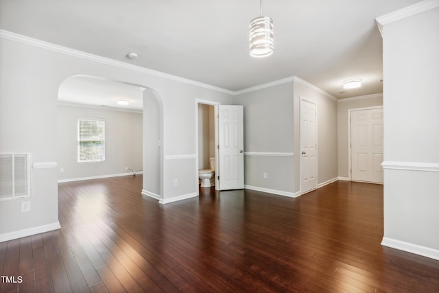 empty room featuring arched walkways, hardwood / wood-style flooring, crown molding, and baseboards