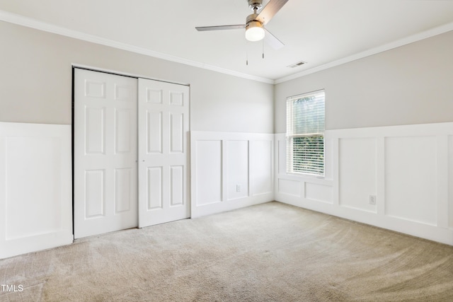 unfurnished bedroom with a decorative wall, crown molding, carpet flooring, wainscoting, and a closet
