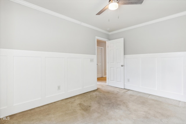 unfurnished room with a decorative wall, carpet floors, crown molding, ceiling fan, and a wainscoted wall