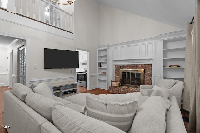 living room with high vaulted ceiling, a brick fireplace, built in shelves, wood finished floors, and crown molding