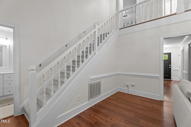 stairway featuring wood finished floors, crown molding, and a high ceiling