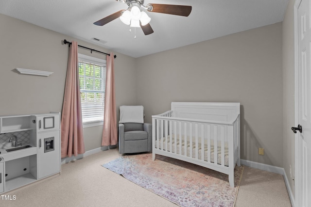 bedroom featuring carpet flooring, a nursery area, baseboards, and a ceiling fan
