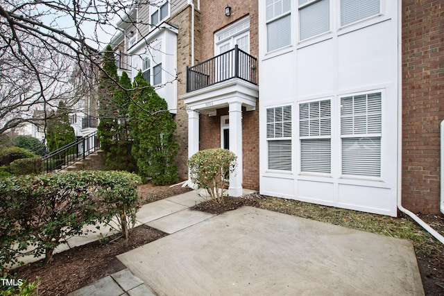 doorway to property with brick siding, a balcony, and a patio