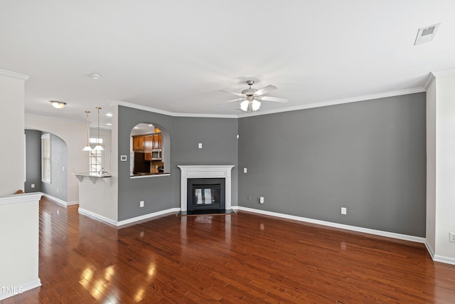 unfurnished living room featuring arched walkways, ceiling fan, wood finished floors, ornamental molding, and baseboards