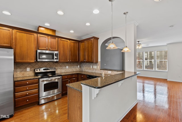 kitchen featuring stainless steel appliances, brown cabinetry, a peninsula, tasteful backsplash, and ceiling fan
