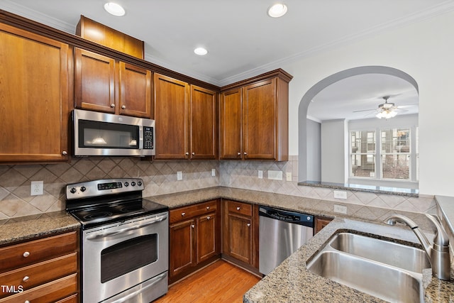 kitchen featuring appliances with stainless steel finishes, a sink, ornamental molding, dark stone counters, and a ceiling fan