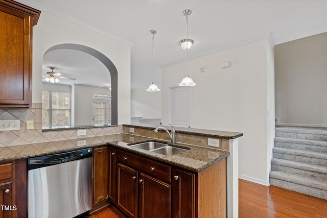 kitchen featuring stainless steel dishwasher, a sink, backsplash, dark stone countertops, and ornamental molding