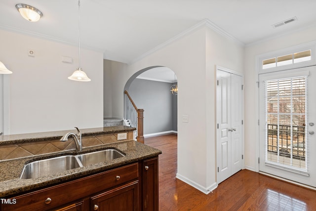 kitchen featuring a sink, arched walkways, dark stone countertops, crown molding, and dark wood finished floors