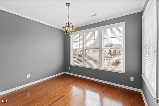 spare room featuring a chandelier, plenty of natural light, baseboards, crown molding, and dark wood finished floors