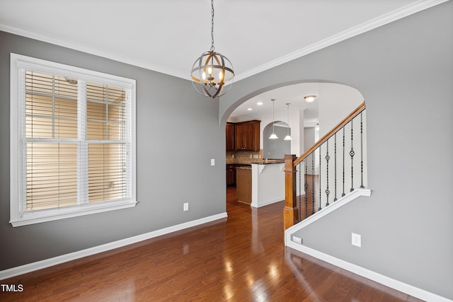empty room featuring arched walkways, dark wood-style flooring, a chandelier, baseboards, and ornamental molding