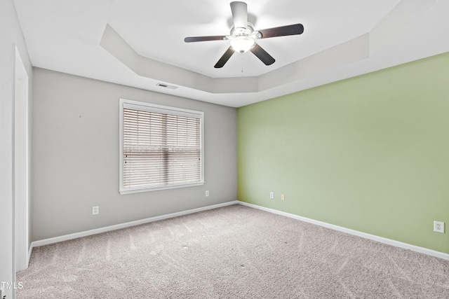 spare room featuring a raised ceiling, carpet floors, and baseboards
