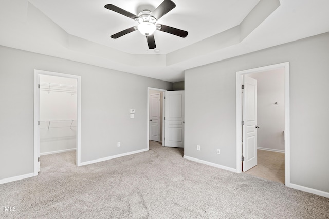 unfurnished bedroom featuring a spacious closet, carpet floors, a tray ceiling, baseboards, and a closet
