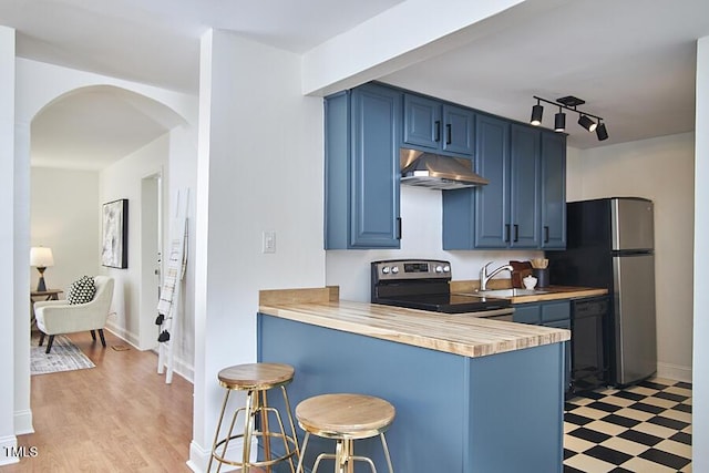 kitchen featuring appliances with stainless steel finishes, under cabinet range hood, blue cabinets, a sink, and a breakfast bar