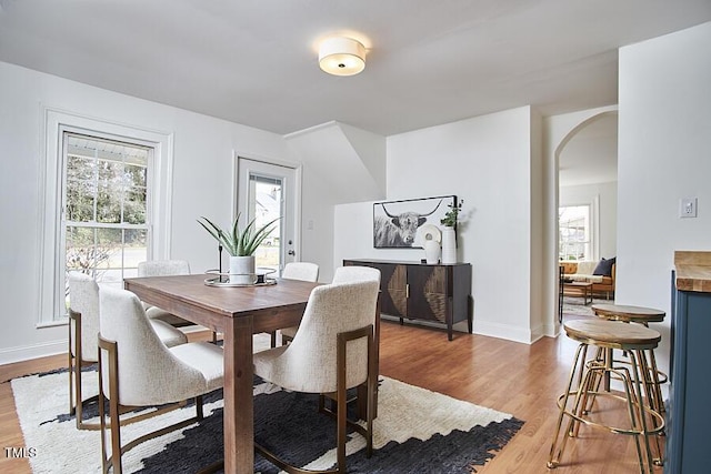 dining space with arched walkways, healthy amount of natural light, wood finished floors, and baseboards