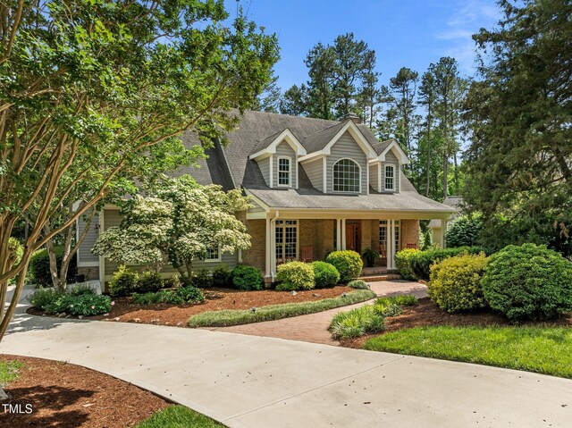 new england style home featuring covered porch, brick siding, and roof with shingles