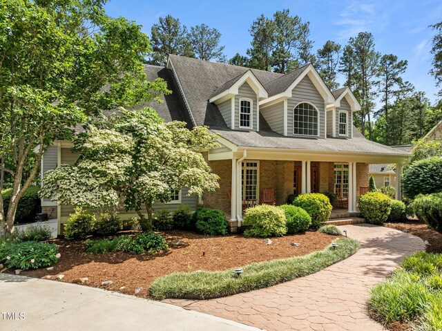 view of front of house with covered porch, brick siding, and a shingled roof