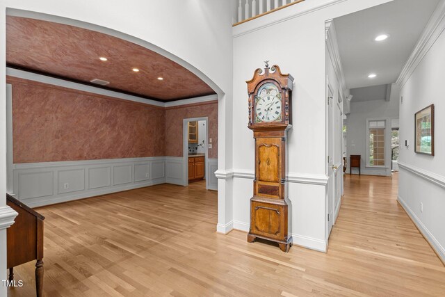 hallway with arched walkways, light wood finished floors, ornamental molding, recessed lighting, and wainscoting
