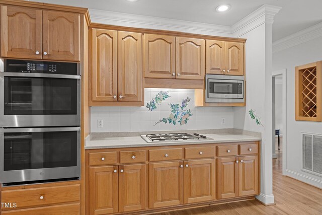 kitchen featuring appliances with stainless steel finishes, light countertops, light wood-style flooring, ornamental molding, and backsplash