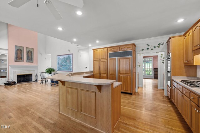 kitchen featuring a ceiling fan, light countertops, a kitchen breakfast bar, paneled refrigerator, and light wood-type flooring