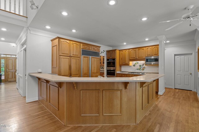 kitchen with crown molding, built in appliances, a breakfast bar area, a peninsula, and light wood finished floors
