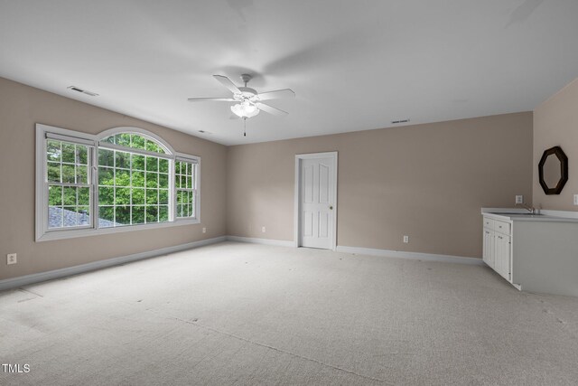 empty room featuring baseboards, a ceiling fan, light colored carpet, and a sink