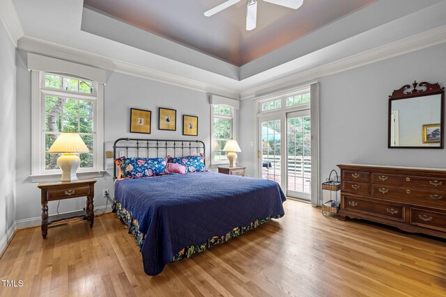 bedroom featuring access to exterior, wood finished floors, multiple windows, a raised ceiling, and crown molding