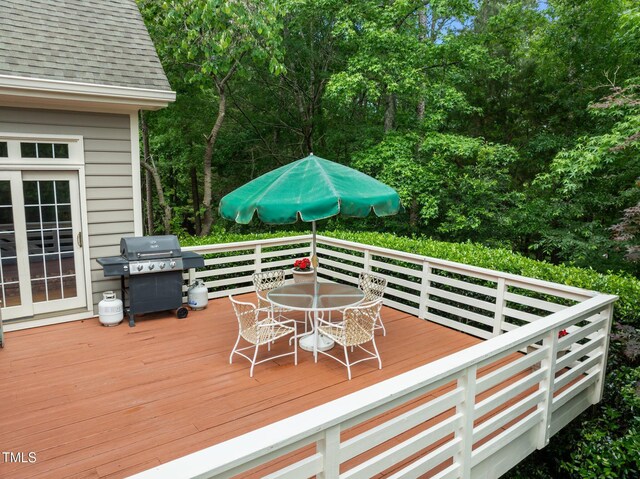 deck featuring outdoor dining space, area for grilling, and view of wooded area