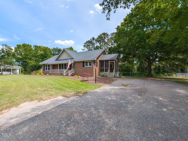 single story home featuring a sunroom, covered porch, brick siding, asphalt driveway, and a front yard