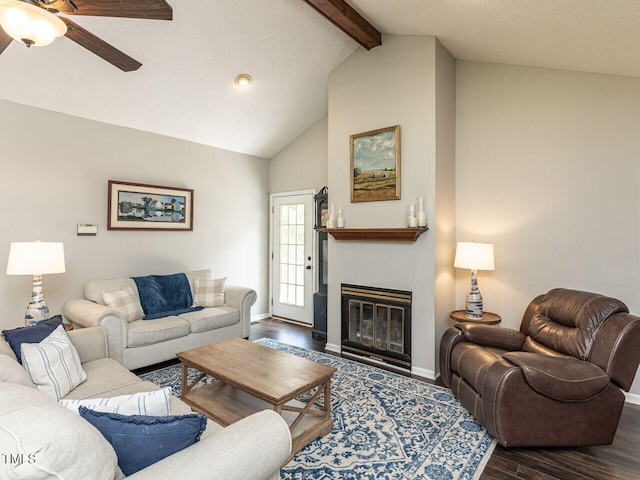 living room featuring a ceiling fan, beam ceiling, wood finished floors, a glass covered fireplace, and baseboards