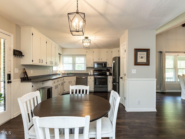 kitchen with appliances with stainless steel finishes, dark countertops, a wainscoted wall, dark wood finished floors, and a textured ceiling