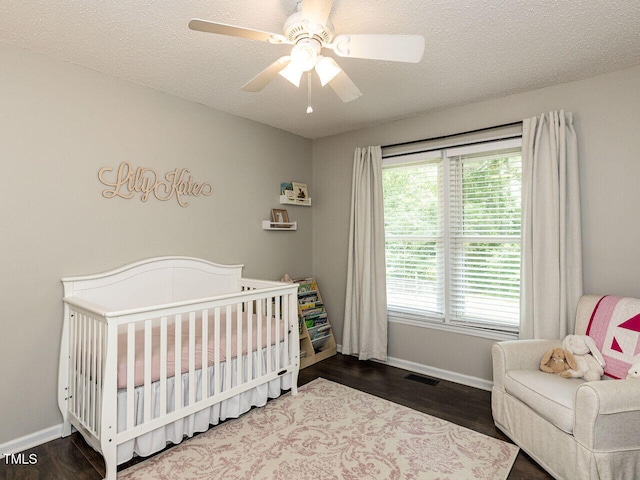 bedroom with a nursery area, baseboards, wood finished floors, and a ceiling fan