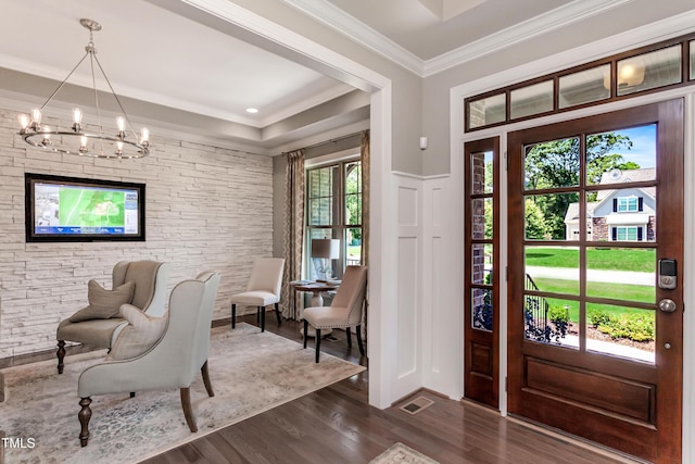 entryway with a chandelier, healthy amount of natural light, dark wood-style floors, a decorative wall, and ornamental molding