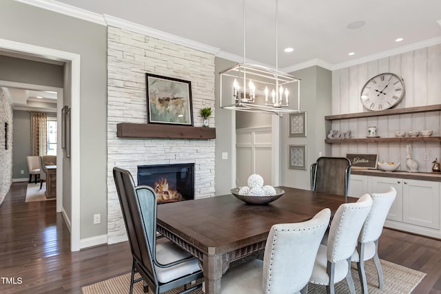 dining area with crown molding, dark wood finished floors, a stone fireplace, a chandelier, and baseboards