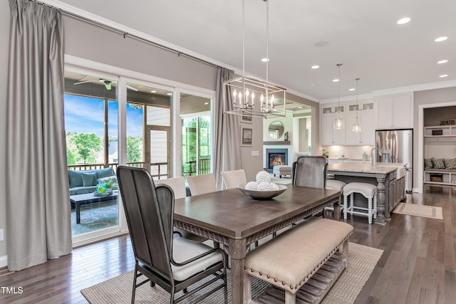 dining space featuring dark wood finished floors, a glass covered fireplace, a chandelier, recessed lighting, and crown molding