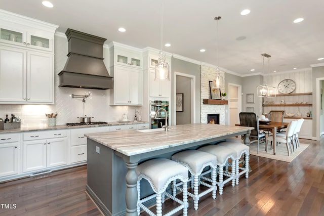kitchen with recessed lighting, premium range hood, appliances with stainless steel finishes, dark wood-style flooring, and a stone fireplace
