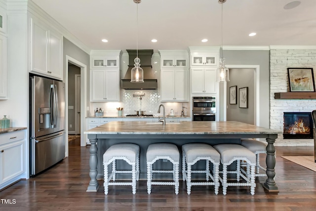 kitchen with appliances with stainless steel finishes, premium range hood, dark wood-style floors, a kitchen breakfast bar, and glass insert cabinets