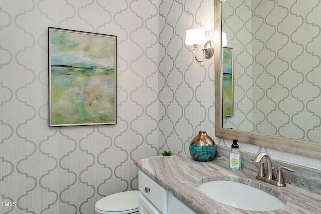 half bath with wallpapered walls, vanity, and toilet