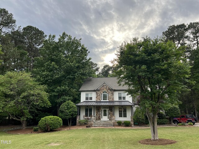 view of front of house with stone siding, a standing seam roof, a front lawn, and metal roof