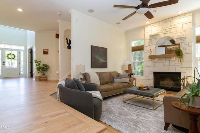 living room featuring a ceiling fan, wood finished floors, stairway, a stone fireplace, and crown molding