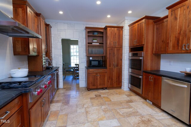 kitchen with appliances with stainless steel finishes, wall chimney exhaust hood, crown molding, dark countertops, and decorative backsplash