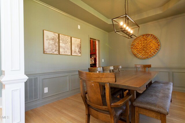 dining area with a decorative wall, a tray ceiling, light wood-type flooring, wainscoting, and crown molding