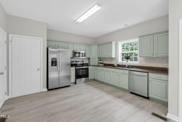 8820 Waynick Dr, Raleigh, NC 27617 - kitchen with appliances with stainless steel finishes, a sink, dark countertops, light wood-style floors, and green cabinetry
