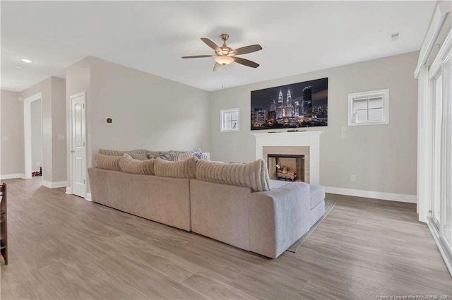 living area featuring ceiling fan, a fireplace, baseboards, and light wood-style flooring
