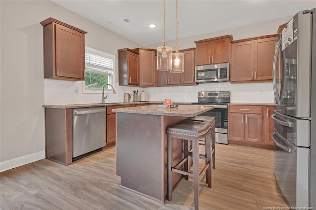kitchen featuring appliances with stainless steel finishes, a sink, light wood-style flooring, a center island, and light stone countertops