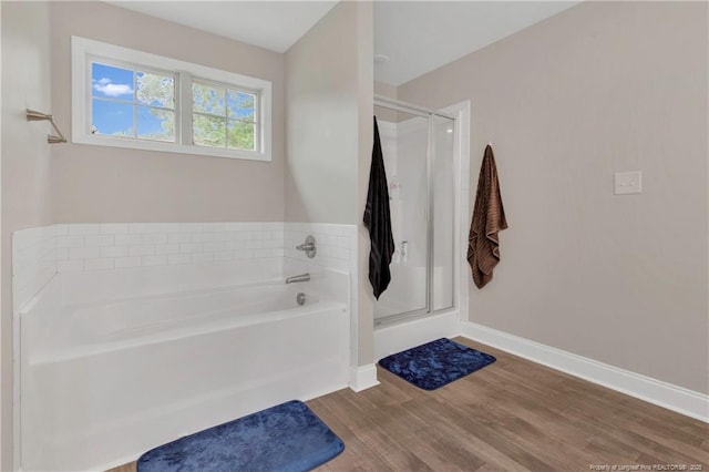 bathroom with wood finished floors, a shower stall, a garden tub, and baseboards
