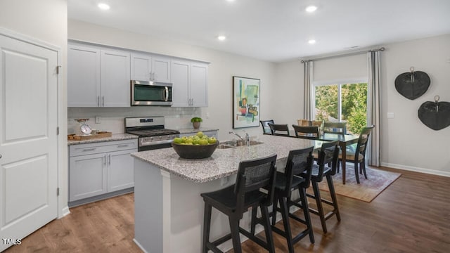 kitchen featuring appliances with stainless steel finishes, a sink, backsplash, dark wood finished floors, and an island with sink