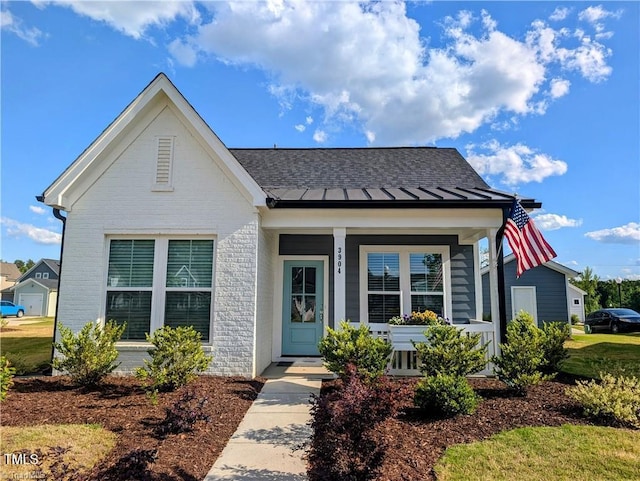 3904 Lundin Dr, Greensboro, NC 27407 - view of front facade with brick siding, covered porch, a shingled roof, and a standing seam roof