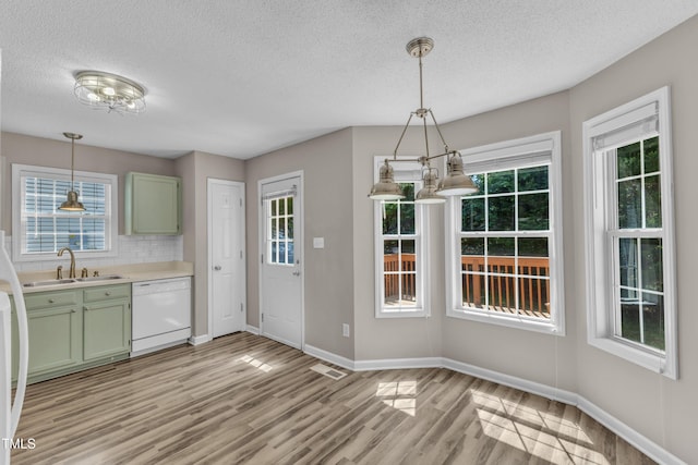 kitchen featuring white dishwasher, green cabinetry, a sink, light wood-style flooring, and baseboards