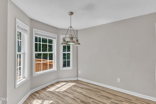 unfurnished dining area with plenty of natural light, wood finished floors, a textured ceiling, and baseboards